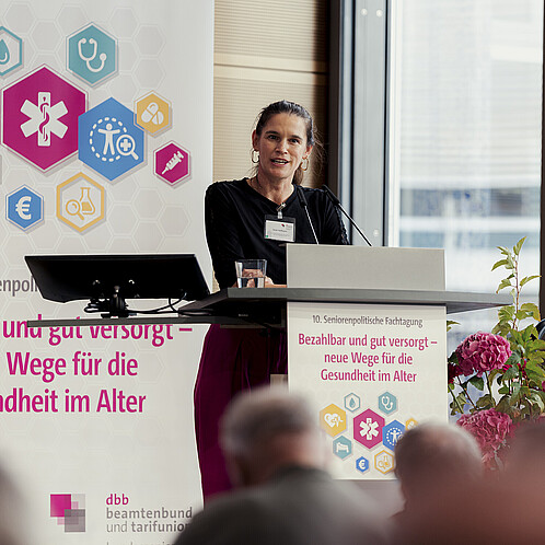 Eine Frau steht hinter einem Rednerpult und spricht in das Mikrofon
