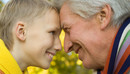 Großvater und Enkelsohn lehnen die Köpfe aneinander und lächeln sich gegenseitig an. 