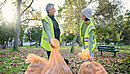 Das Foto zeigt zwei Frauen im Park, die sich freiwillig engagieren und Müll einsammeln.