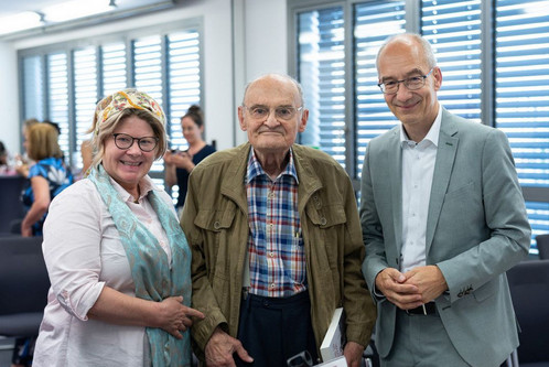 Drei Menschen stehen in einem Tagungsraum und blicken in die Kamera