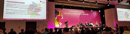 Mehrere Menschen sitzen auf einer Bühne in Stühlen und diskutieren miteinander