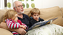 people, person, scandinavian, adult, child, male, man, senior, grandfather, grandparent, girl, boy, grandchild, group, age, 60, 3, 5, sitting, sofa, inside, indoors, livingroom, home, daylight, family, generation, togetherness, love, harmony, loving, reading, book, story, telling, enjoying, feeling, tenderness, happiness, happy, joyful, joy, entertainment, entertaining, blond, grey, casual, relaxed, relaxing, lifestyle, wellness