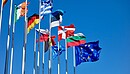 Verschiedene europäische Landesflaggen sowie eine EU-Flagge an Fahnenmasten wehen im Wind.