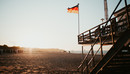 An einen Stelzenhaus am Strand ist die Deutschlandflagge gehisst, im Hintergrund scheint die Abendsonne. 