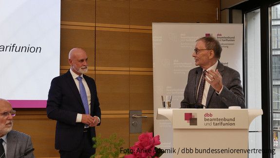 Zwei Männer in Anzügen unterhalten sich auf einer Bühne.