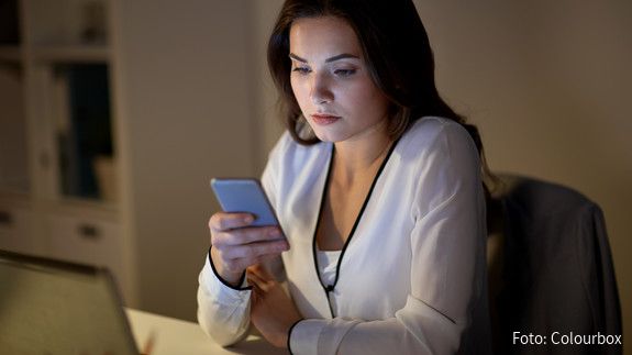 Whistleblower Eine junge Frau im Büro sieht mit ernstem Gesichtsausdruck auf das Display ihres Handys.