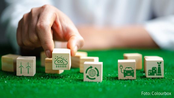 Grüner Wandel Nahaufnahme einer Hand, die auf einer grünen Fläche verschiedene Würfel mit Symbolen für erneuerbare Energien platziert.