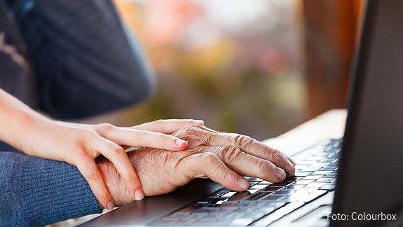 Die Hand einer älteren Person liegt auf dem Mauspad eines Laptops. Auf der Hand liegt die eine jüngeren Person.