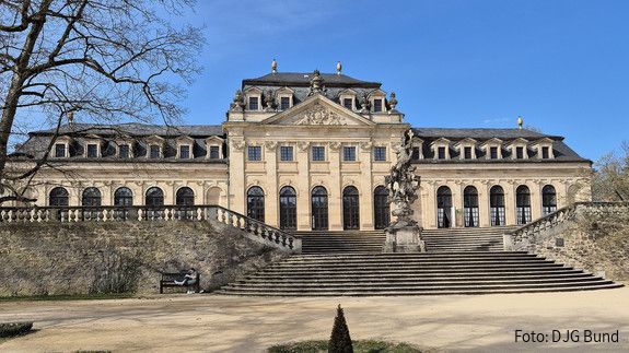 Ein barocker Palast mit blauem Himmel im Hintergrund und einer Parkanlage im Vordergrund