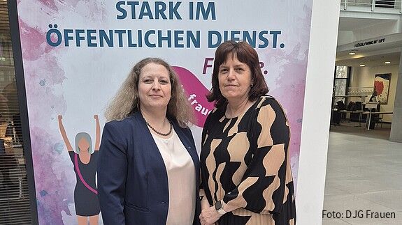 Zwei Frauen in formaler Kleidung stehen vor einem pinken Aufsteller
