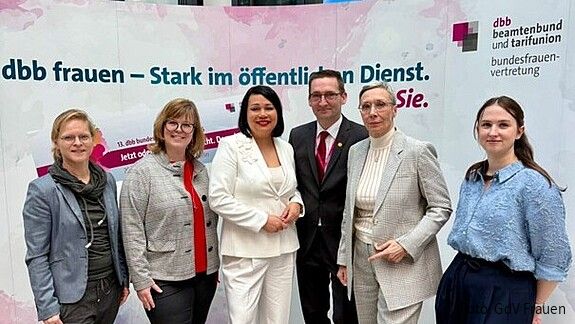 fünf frauen und ein Mann stehen vor einem rosa Aufsteller