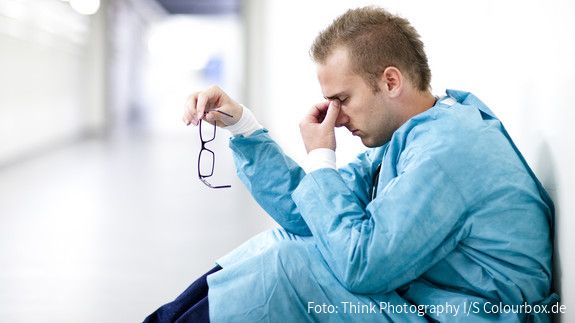 Arzt sitzt erschöpft am Boden