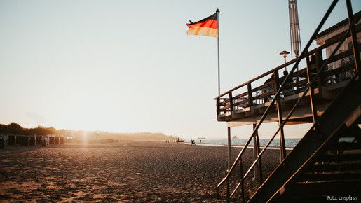 An einen Stelzenhaus am Strand ist die Deutschlandflagge gehisst, im Hintergrund scheint die Abendsonne. 
