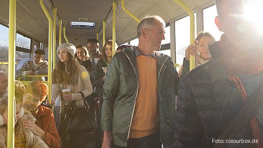 Blick in den Innenraum eines Busses auf stehende und sitzende Passagiere aus allen Altersgruppen
