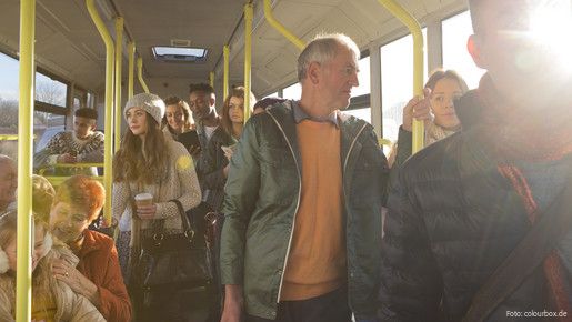 Blick in den Innenraum eines Busses auf stehende und sitzende Passagiere aus allen Altersgruppen