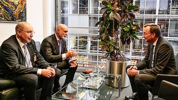 Drei Männer sitzen in einem Büro und diskutieren miteinander