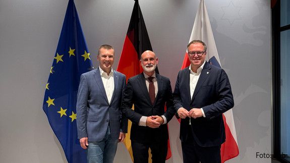 Drei Männer in Anzügen stehen vor einer EU-, Deutschland- und Thüringenflagge und blicken lächelnd in die Kamera