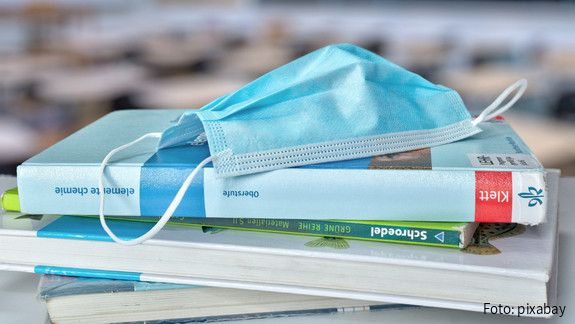 Stapel Schulbücher, auf dem eine medizinische Maske liegt